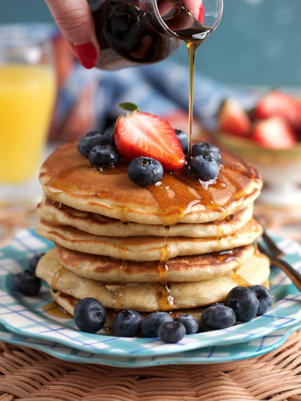 Stack of sourdough pancakes on a plaid plate with syrup being drizzled over top.