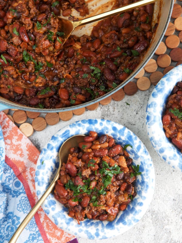 dutch oven with cowboy beans and a serving spoon, two bowls with a serving of cowboy beans next to it.