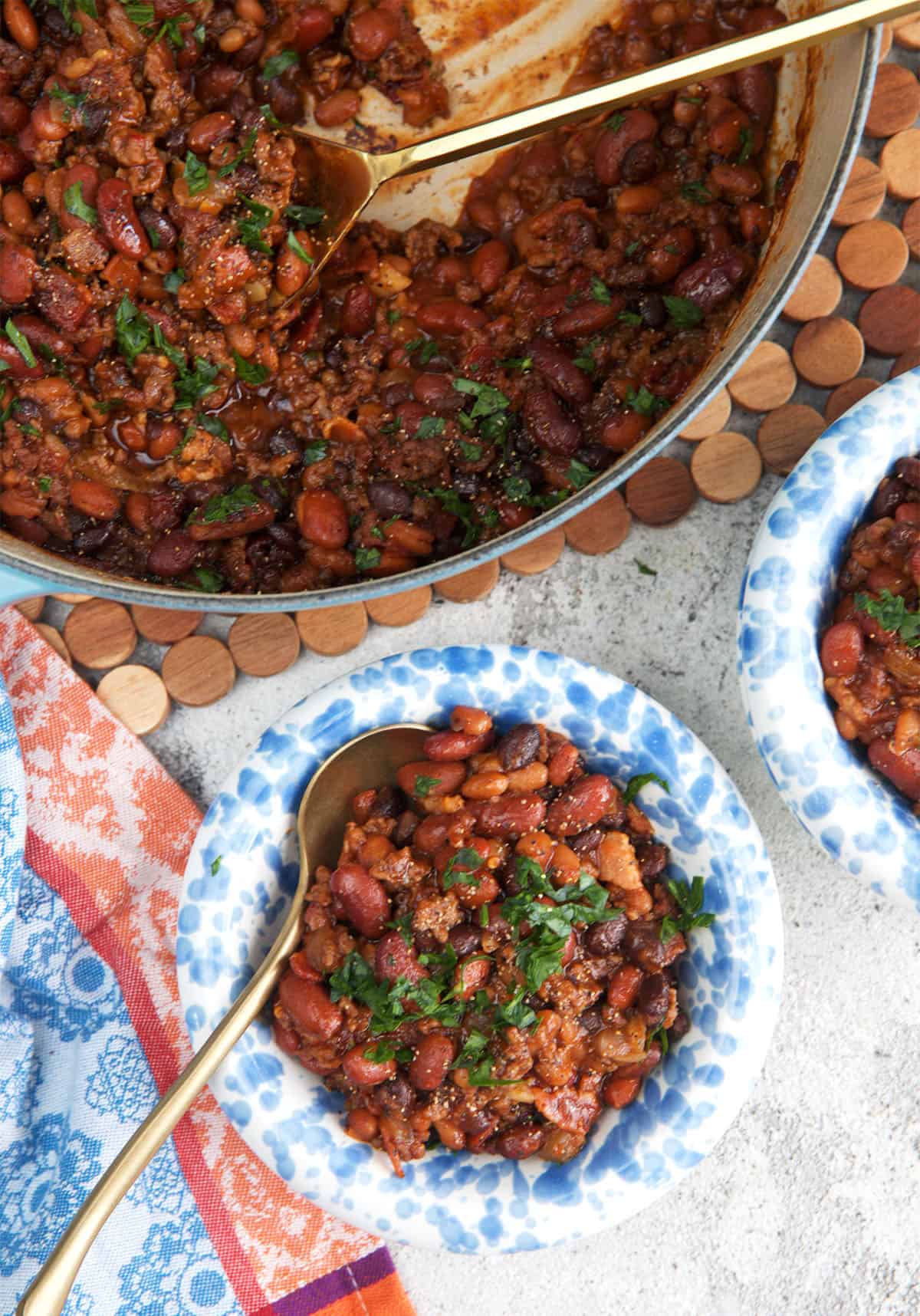 dutch oven with cowboy beans and a serving spoon, two bowls with a serving of cowboy beans next to it.