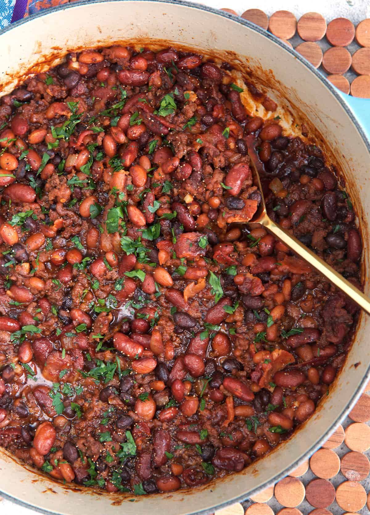 Cowboy beans in a large dutch oven with a gold serving spoon
