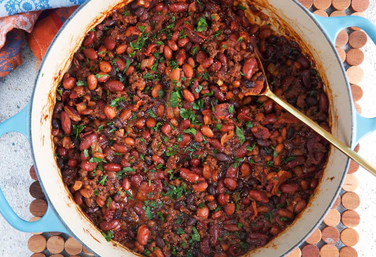 Easy Cowboy beans in a large dutch oven topped with parsley and a serving spoon.