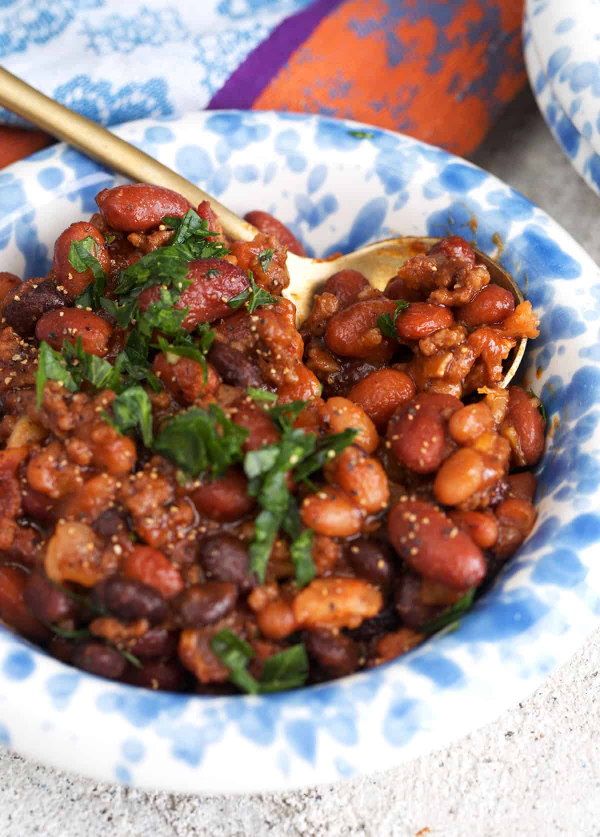 Cowboy beans in a blue and white spatter bowl with a gold spoon.