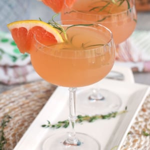 French Blonde Cocktail in a fluted coupe glass on a white platter with a thyme sprig