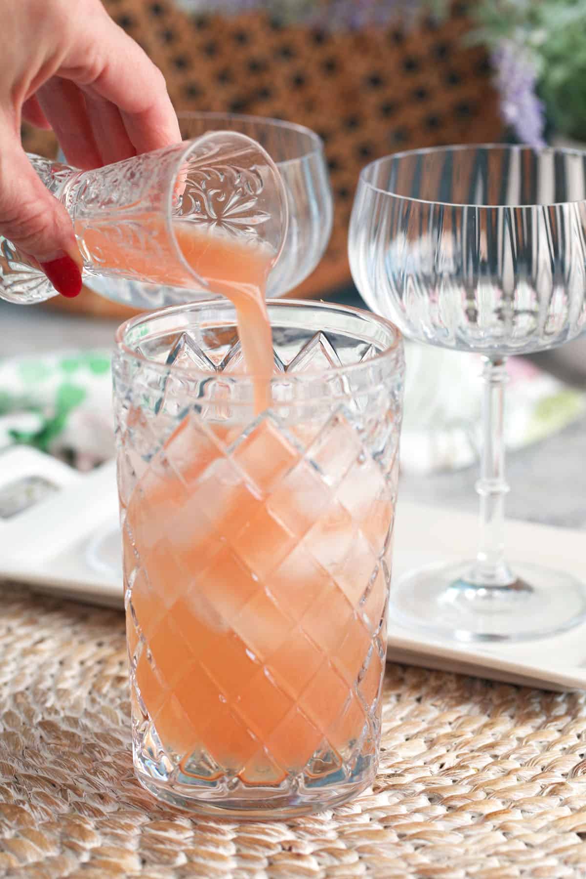 grapefruit juice being poured into a cocktail shaker with a crystal jigger