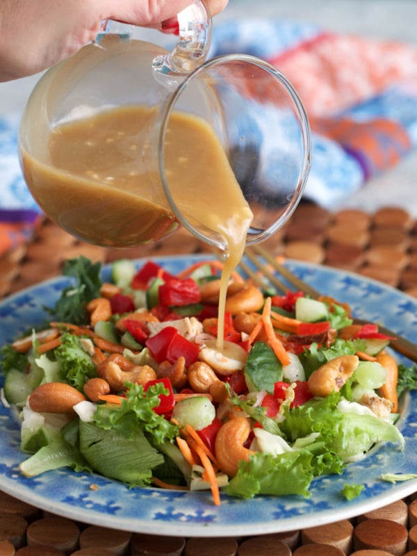 Miso salad dressing being poured over an asian inspired salad.