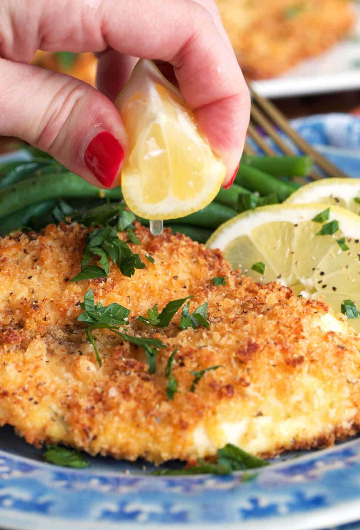 lemon squeezed over crispy baked tilapia on a plate.