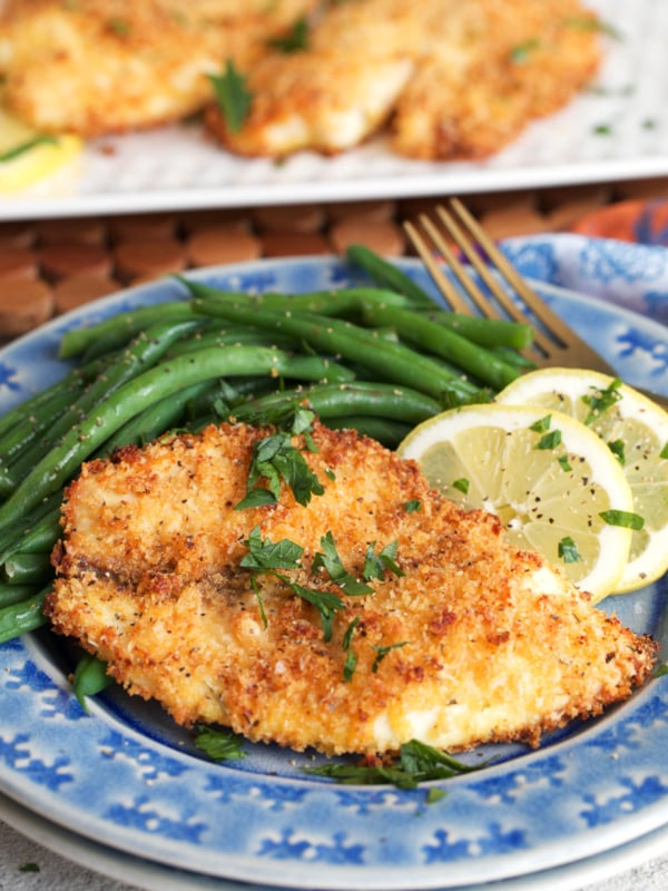 parmesan crusted tilapia with green beans and a lemon on a blue plate.