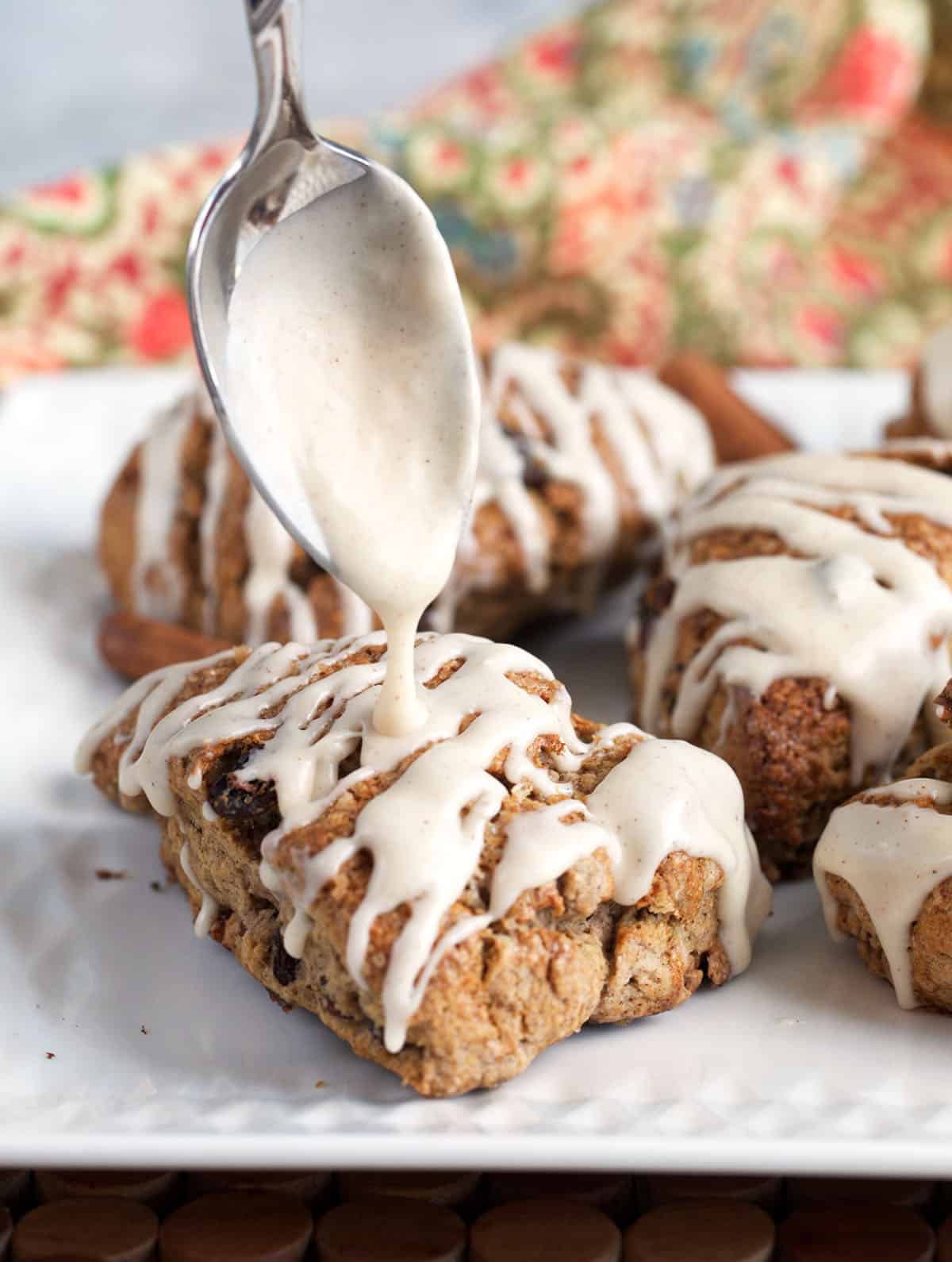 Glaze being drizzled over a sourdough scone with a spoon while plated on a white platter.
