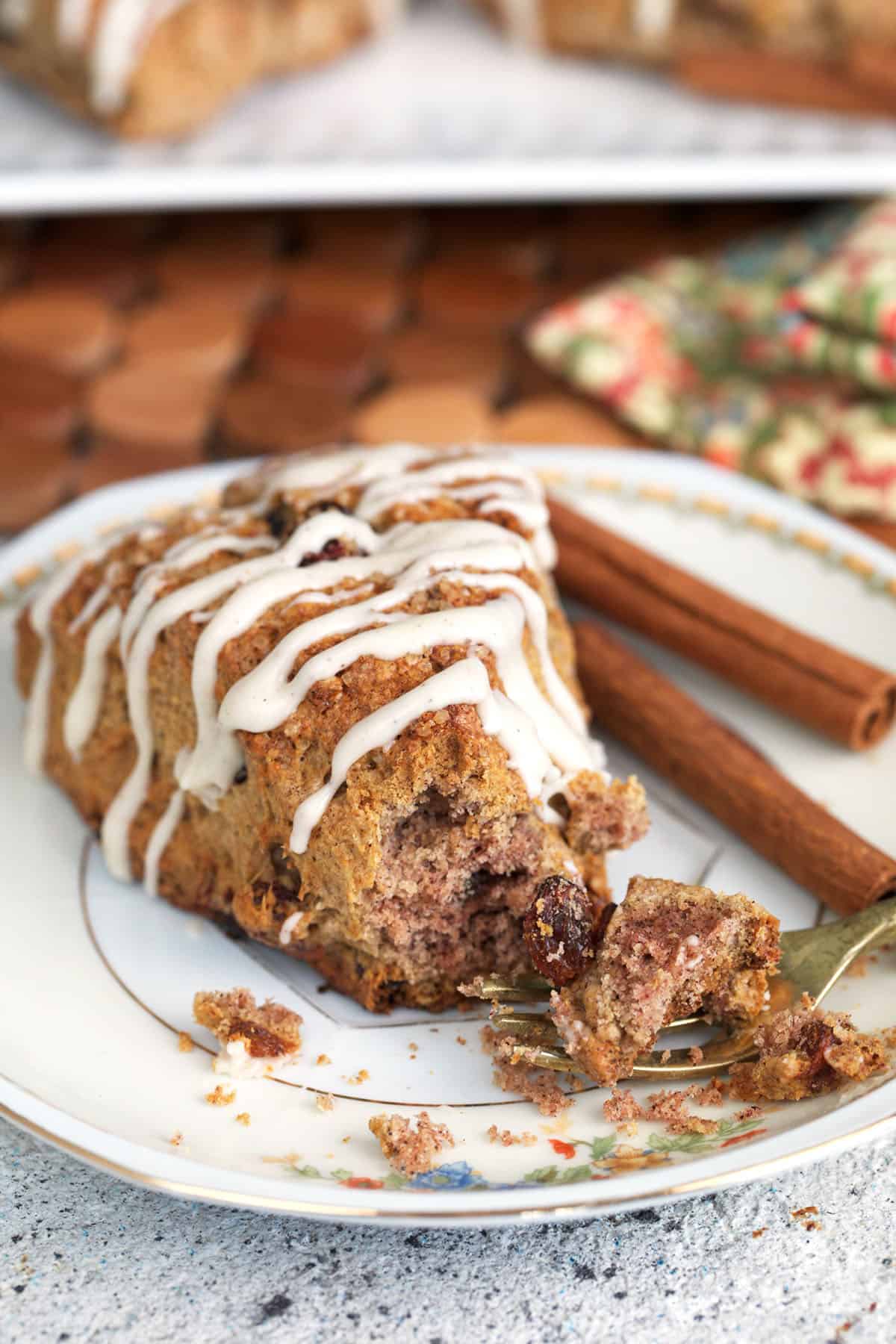 Sourdough scone with cinnamon and raisins on a plate with cinnamon sticks and a gold pastry fork.