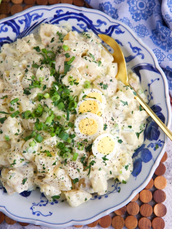 Amish potato salad in a blue and white serving bowl with a gold serving spoon