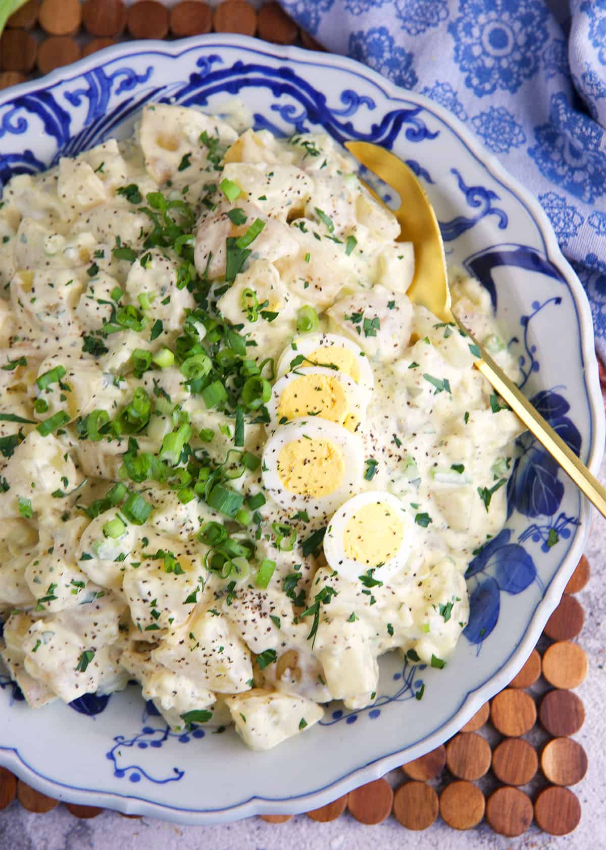 Amish potato salad in a blue and white serving bowl with a gold serving spoon