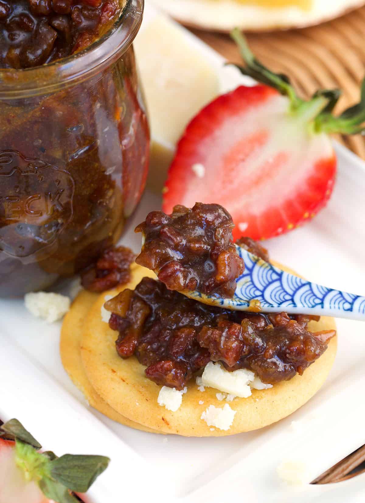 Bacon jam being spread on a cracker with a blue and white serving spoon