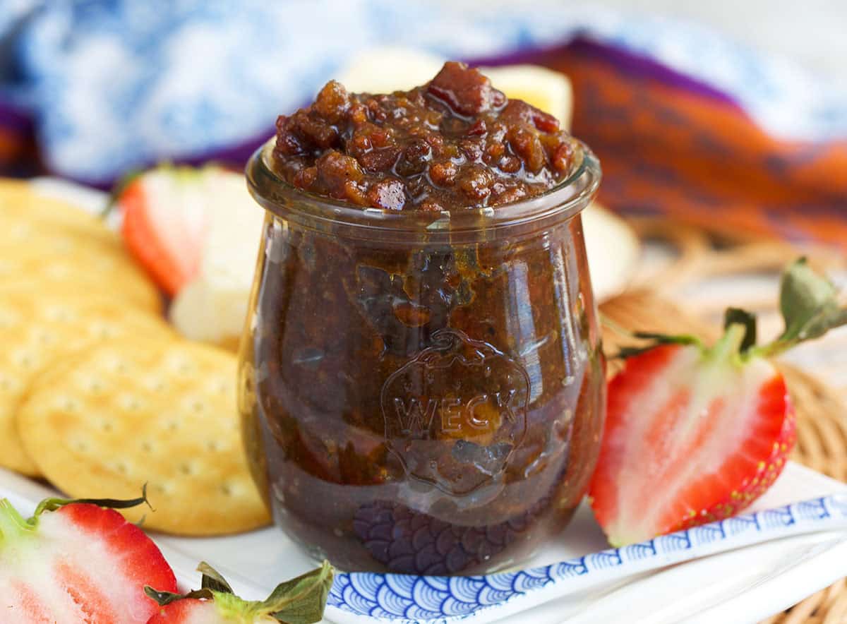 Bourbon bacon jam on a white tray with strawberries and crackers.