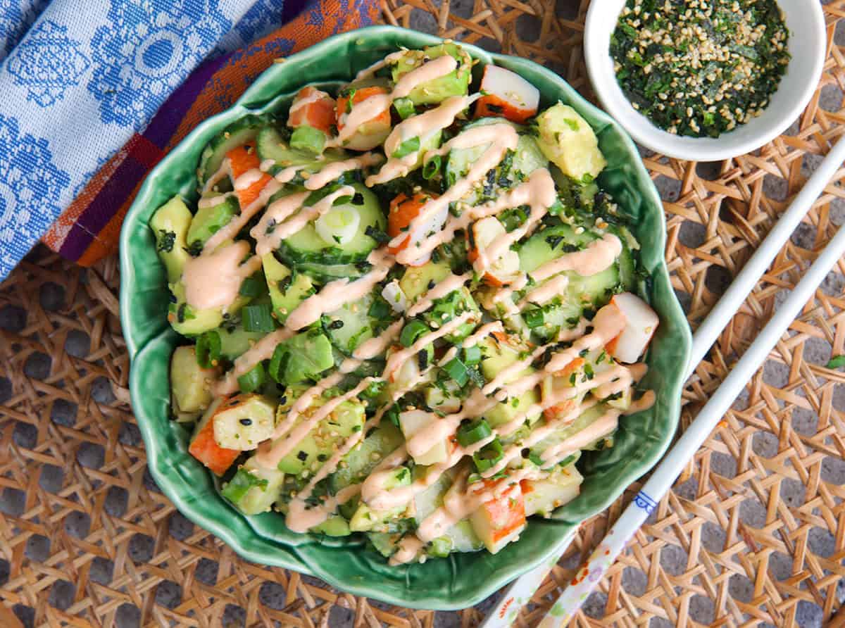 California Roll Cucumber salad topped with spicy mayo and nori flakes in a bowl with white chopsticks.