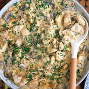 Chicken stroganoff recipe in a large skillet with a wooden spoon for serving.