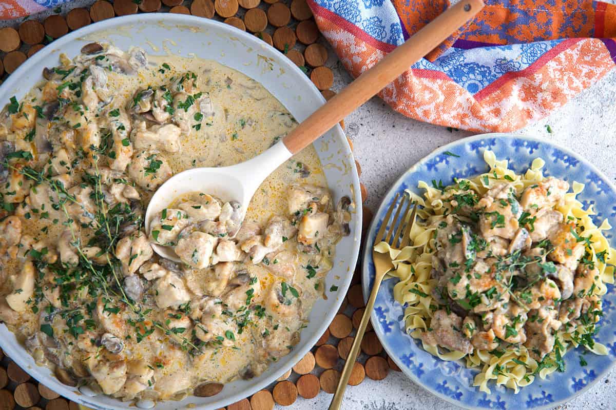 Chicken stroganoff in a skillet and served over egg noodles on a blue plate.