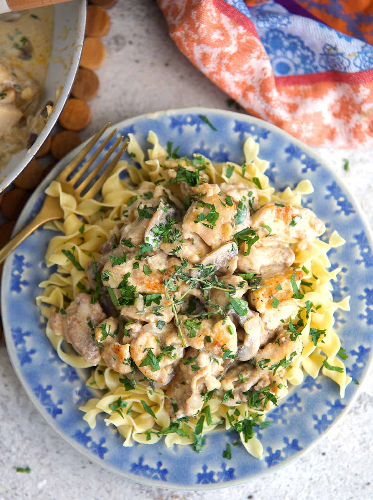 Chicken stroganoff over egg noodles on a blue plate.