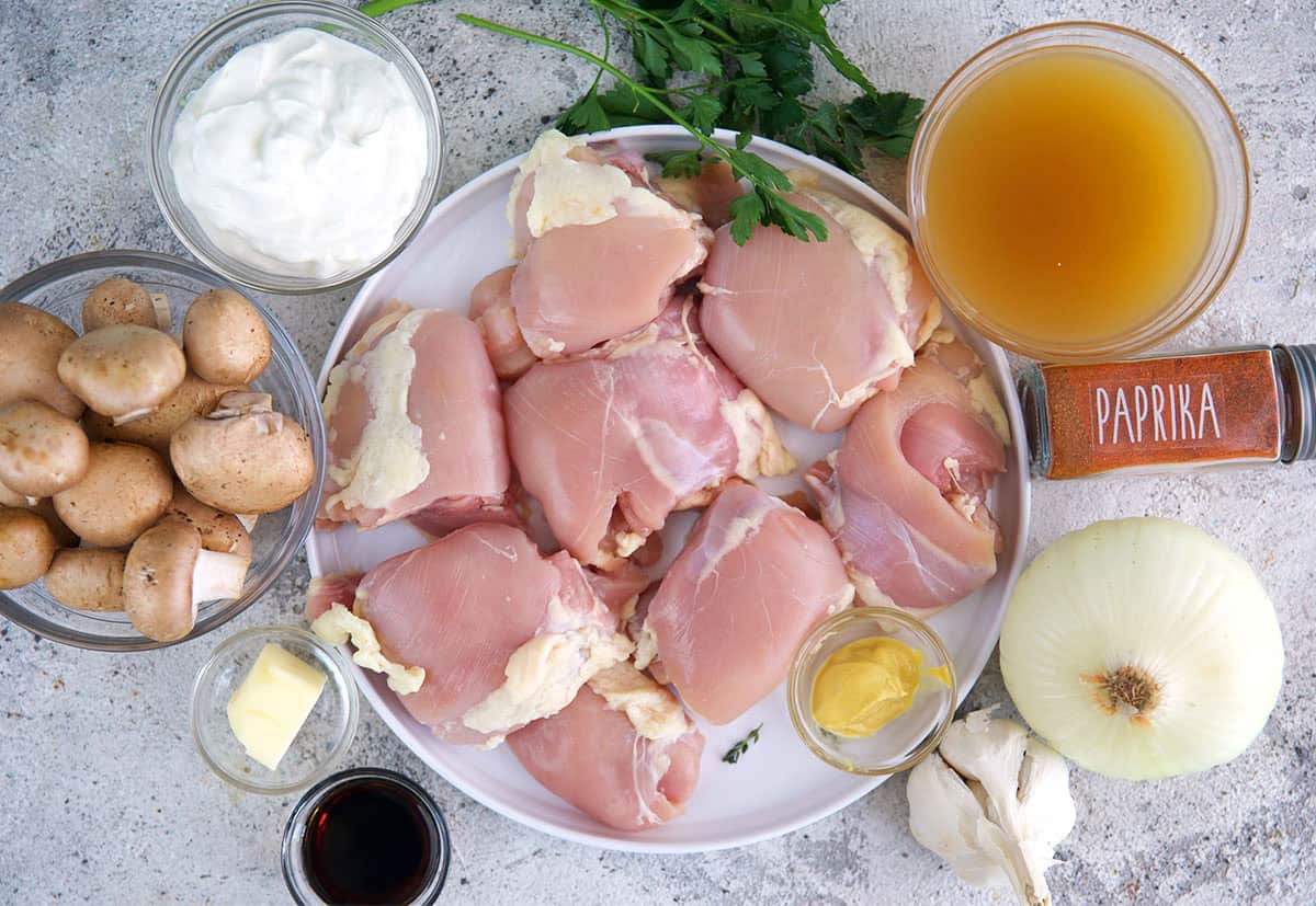 Ingredients for chicken stroganoff, chicken thighs, mushrooms, sour cream, chicken stock, seasonings, onion and garlic.