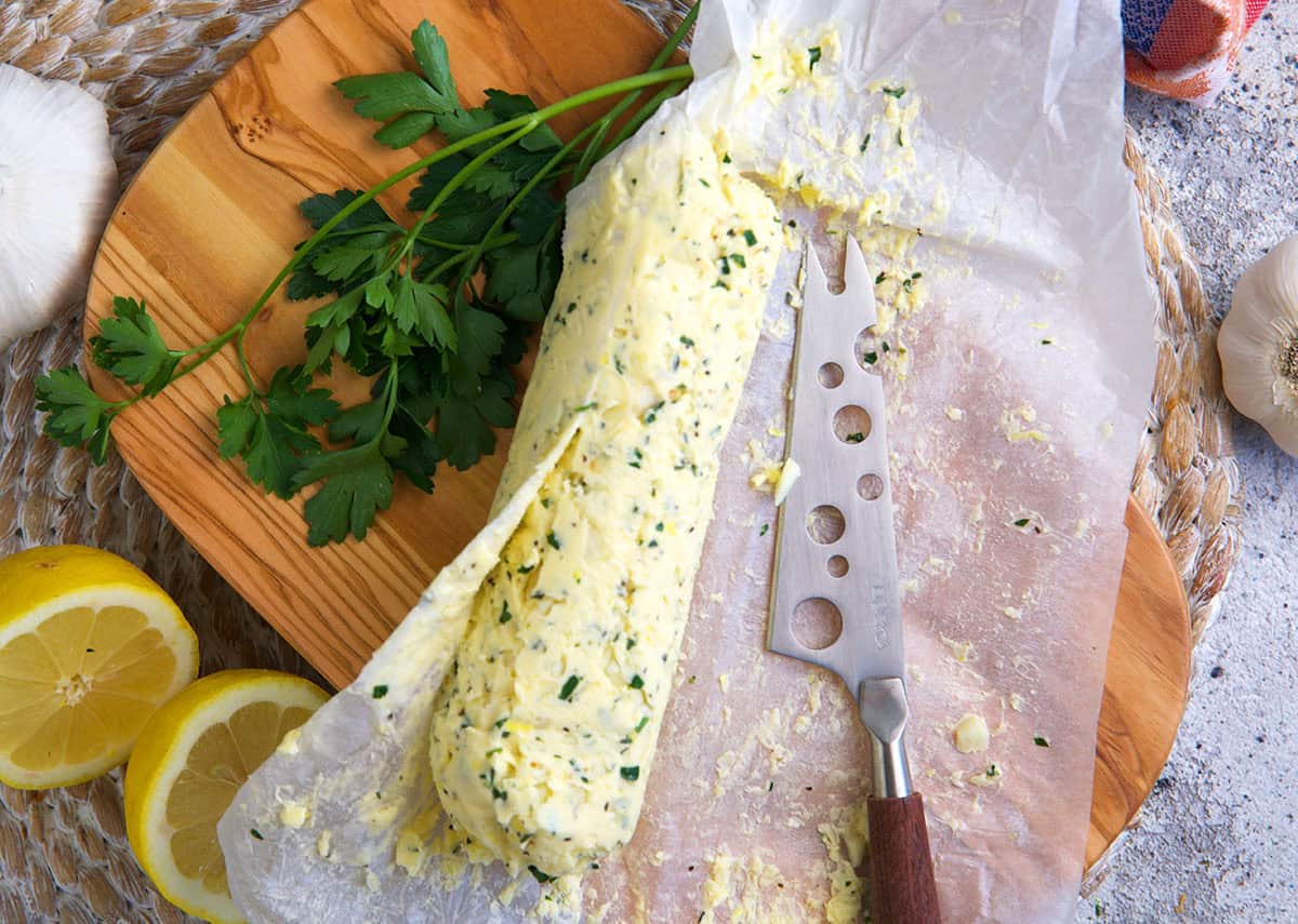 cowboy butter slightly unrolled from parchment wrapper with a cheese knife for slicing.