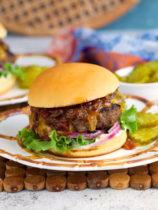 Crack burger on a white plate with a side of pickles.