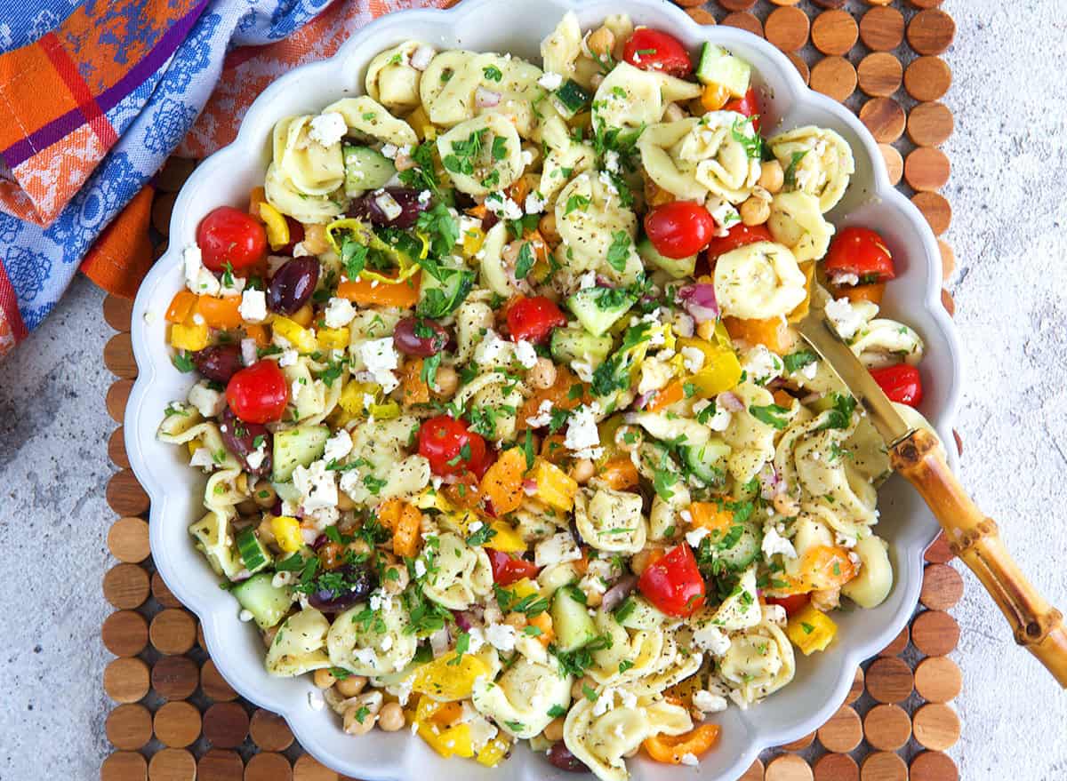 Greek Tortellini Pasta Salad in a white serving bowl with a bamboo serving spoon.