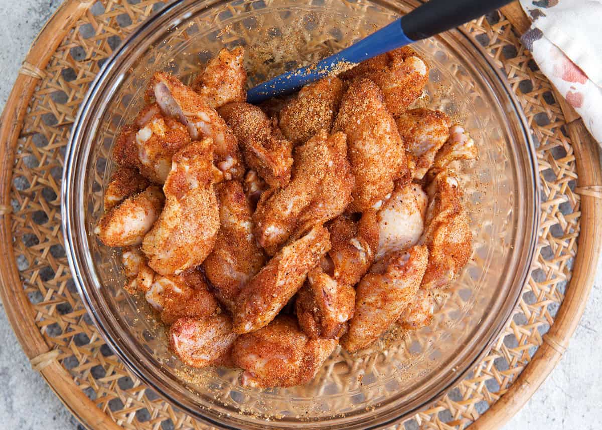 chicken wings in a glass mixing bowl being tossed with seasoning.
