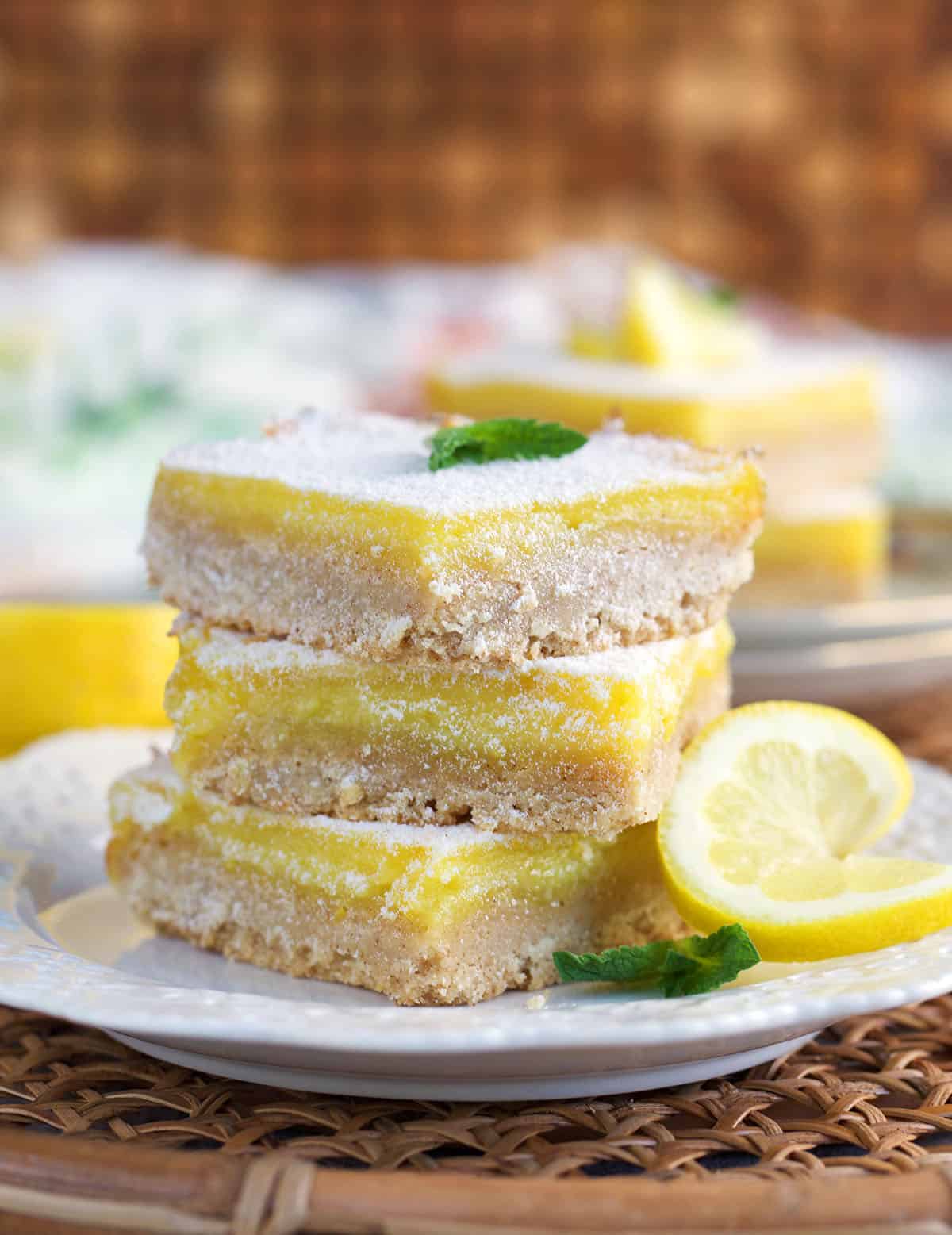 stack of lemon bar cookies on a plate and topped with a sprig of mint.