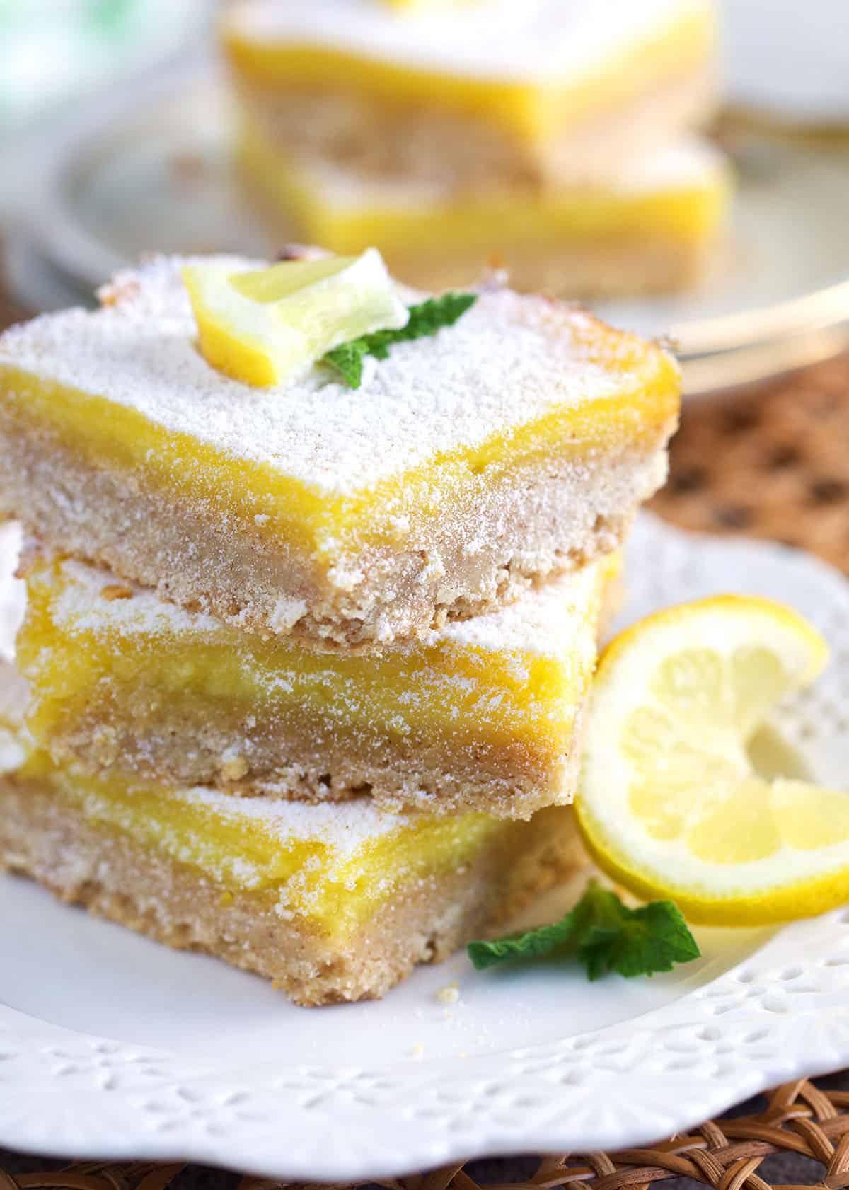 Lemon Bars stacked on a white plate and dusted with powdered sugar.