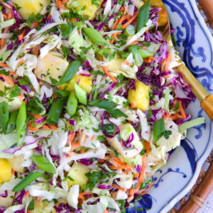 Pineapple coleslaw in a blue and white serving bowl with a gold serving spoon.