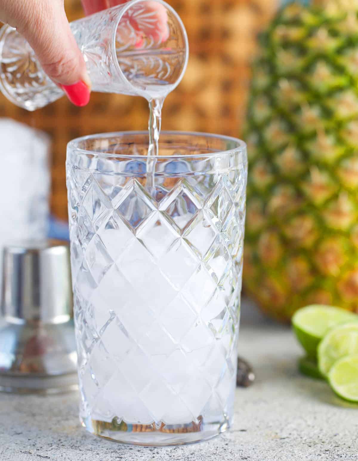 cocktail shaker with tequila being poured into it for pineapple margarita