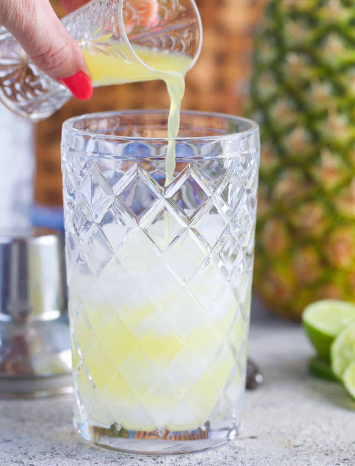 pineapple juice being poured into a cocktail shaker with ice