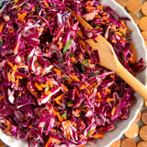 Red Cabbage slaw in a white serving bowl with a wooden serving fork.