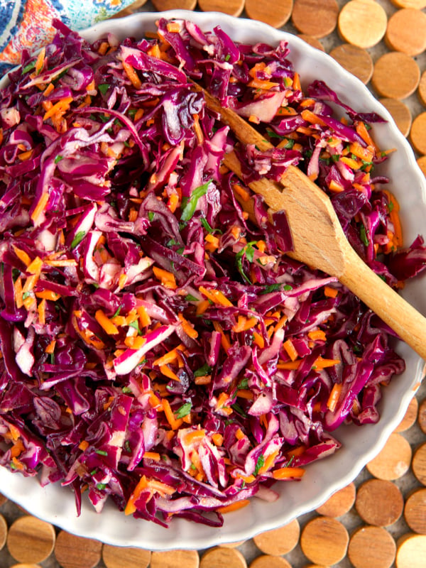 Red Cabbage slaw in a white serving bowl with a wooden serving fork.
