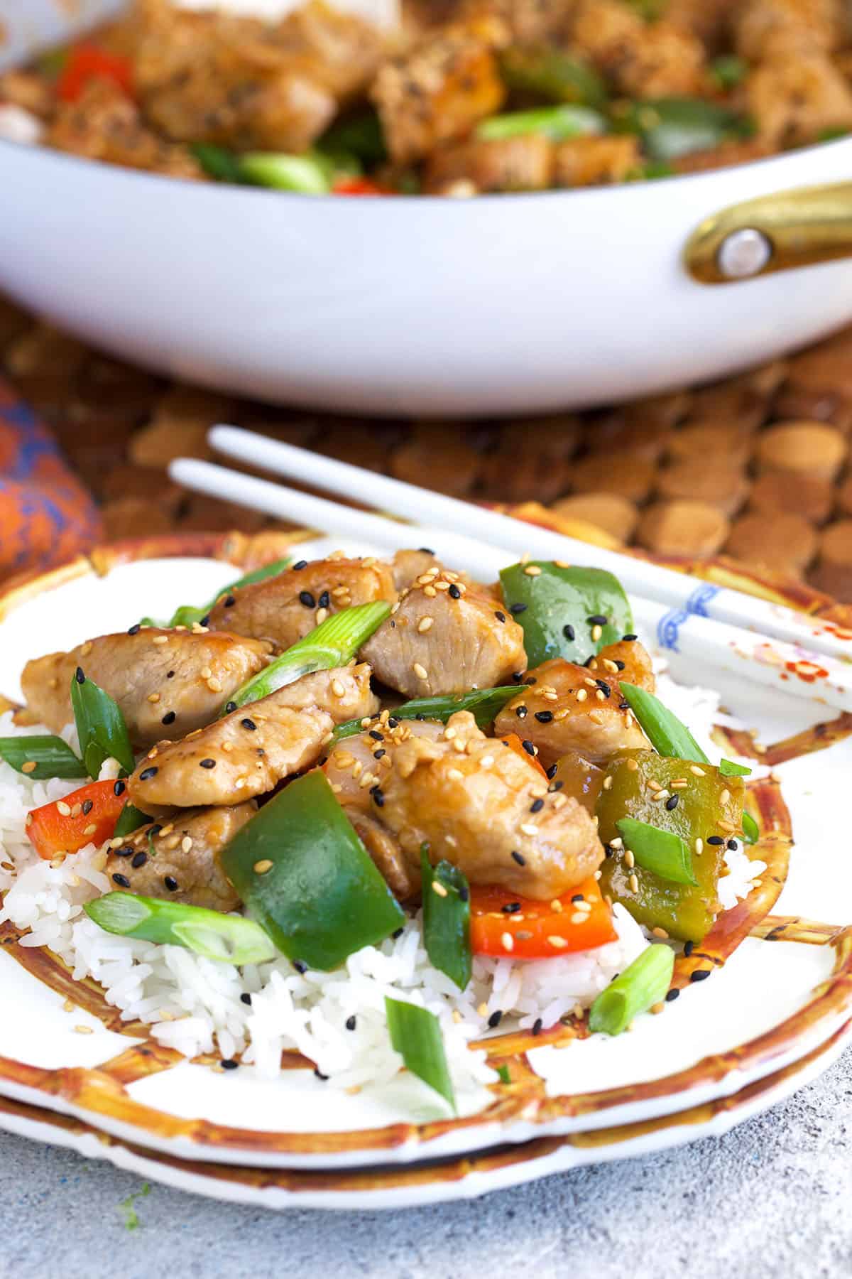 sweet and sour pork plated on a bamboo and white plate over rice with white chop sticks.