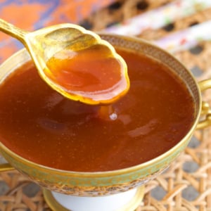 sweet and sour sauce in a compote dish with a gold spoon.