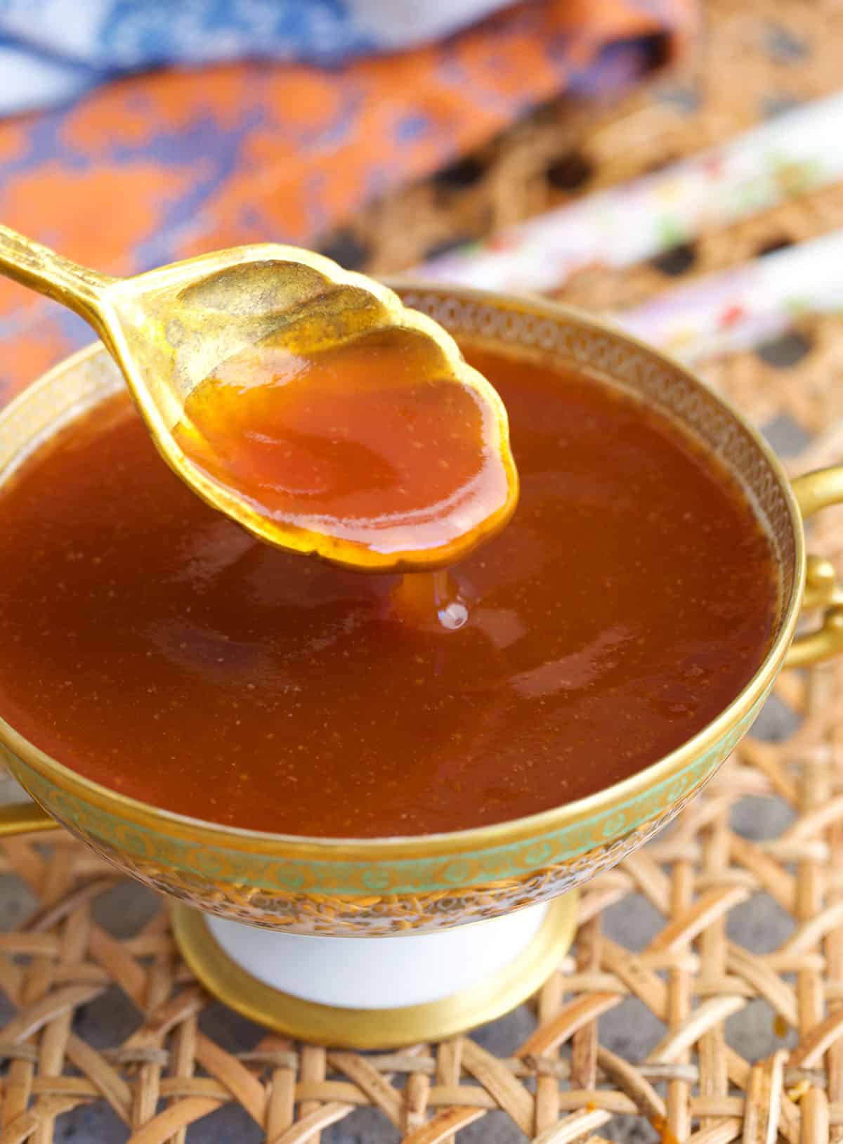 sweet and sour sauce in a compote dish with a gold spoon.