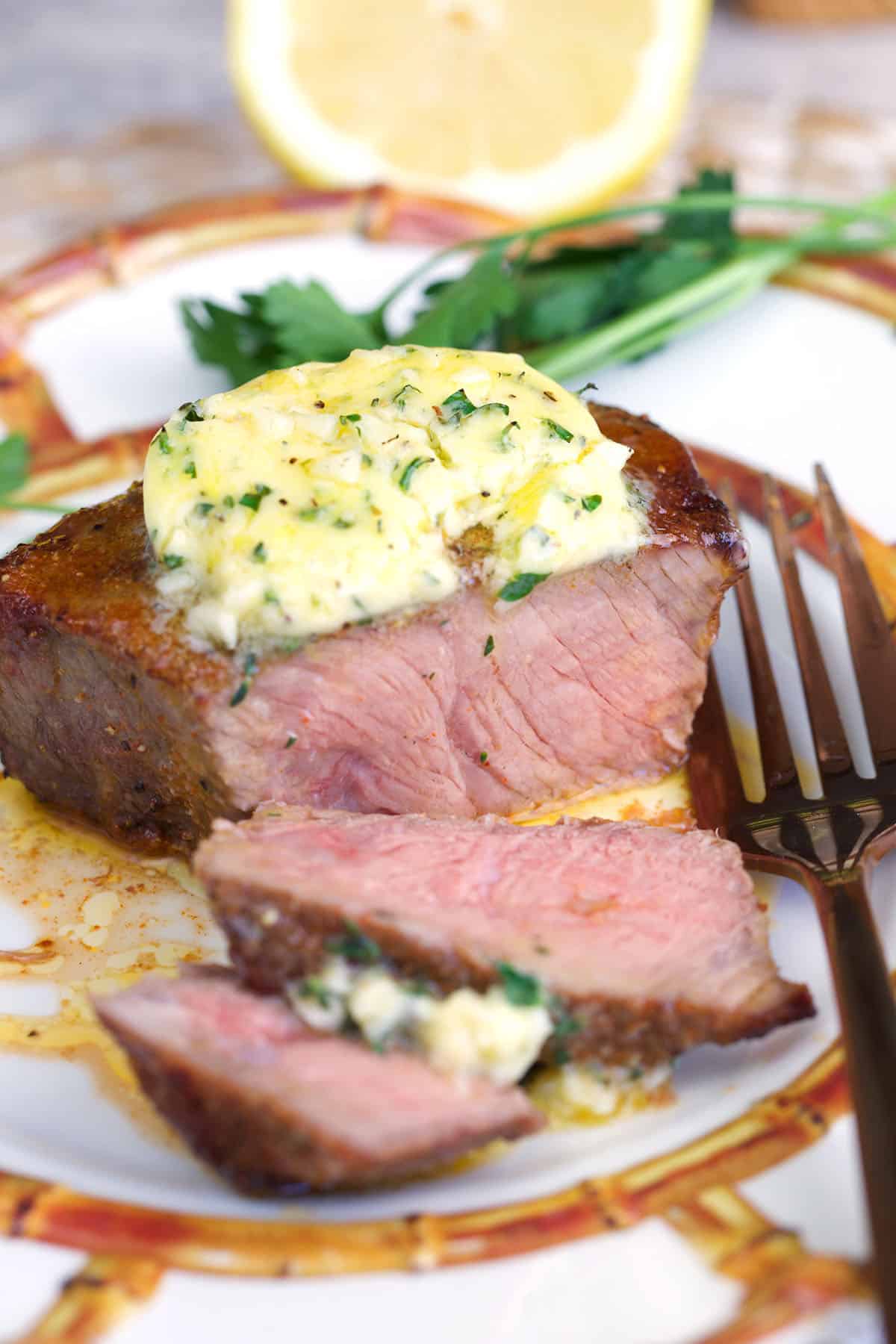 Air fryer sirloin steak topped with cowboy butter on a plate with a fork.