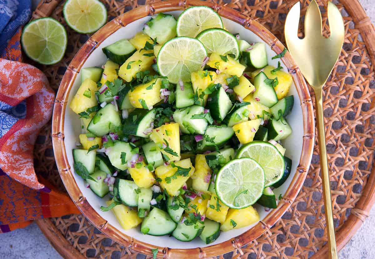 Pineapple cucumber salad with pineapple vinaigrette in a melamine bamboo bowl and a gold serving spoon along the side.