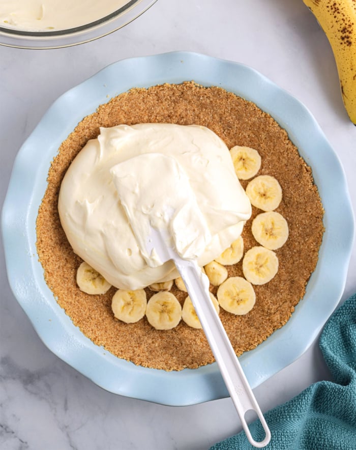 bananas on the cookie pie crust with cream being spread on top
