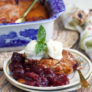 Cherry cobbler on a plate topped with a scoop of vanilla ice cream and a sprig of mint.
