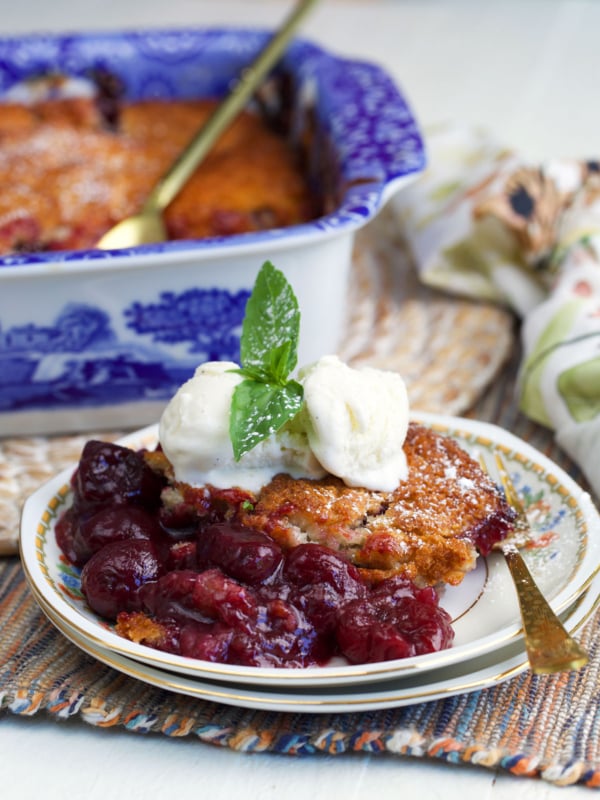 Cherry cobbler on a plate topped with a scoop of vanilla ice cream and a sprig of mint.