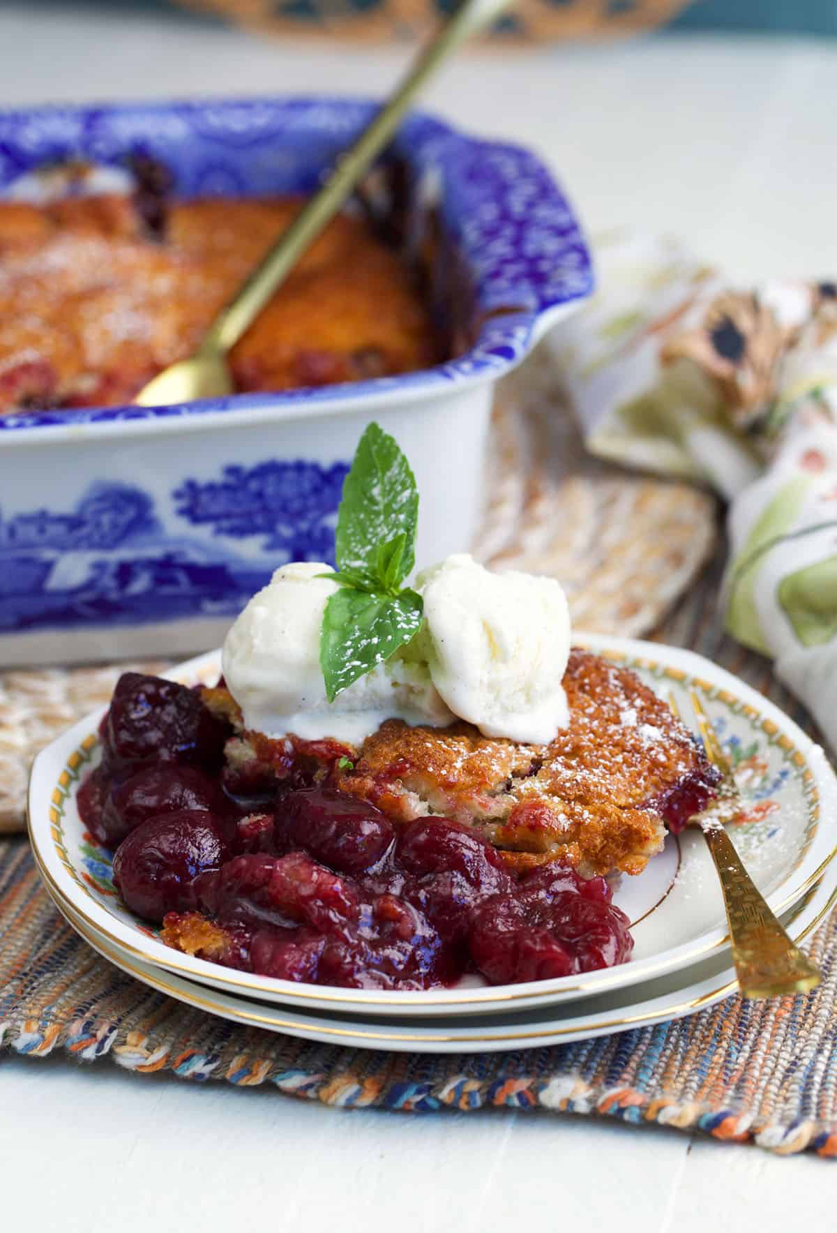 Cherry cobbler on a plate topped with a scoop of vanilla ice cream and a sprig of mint.