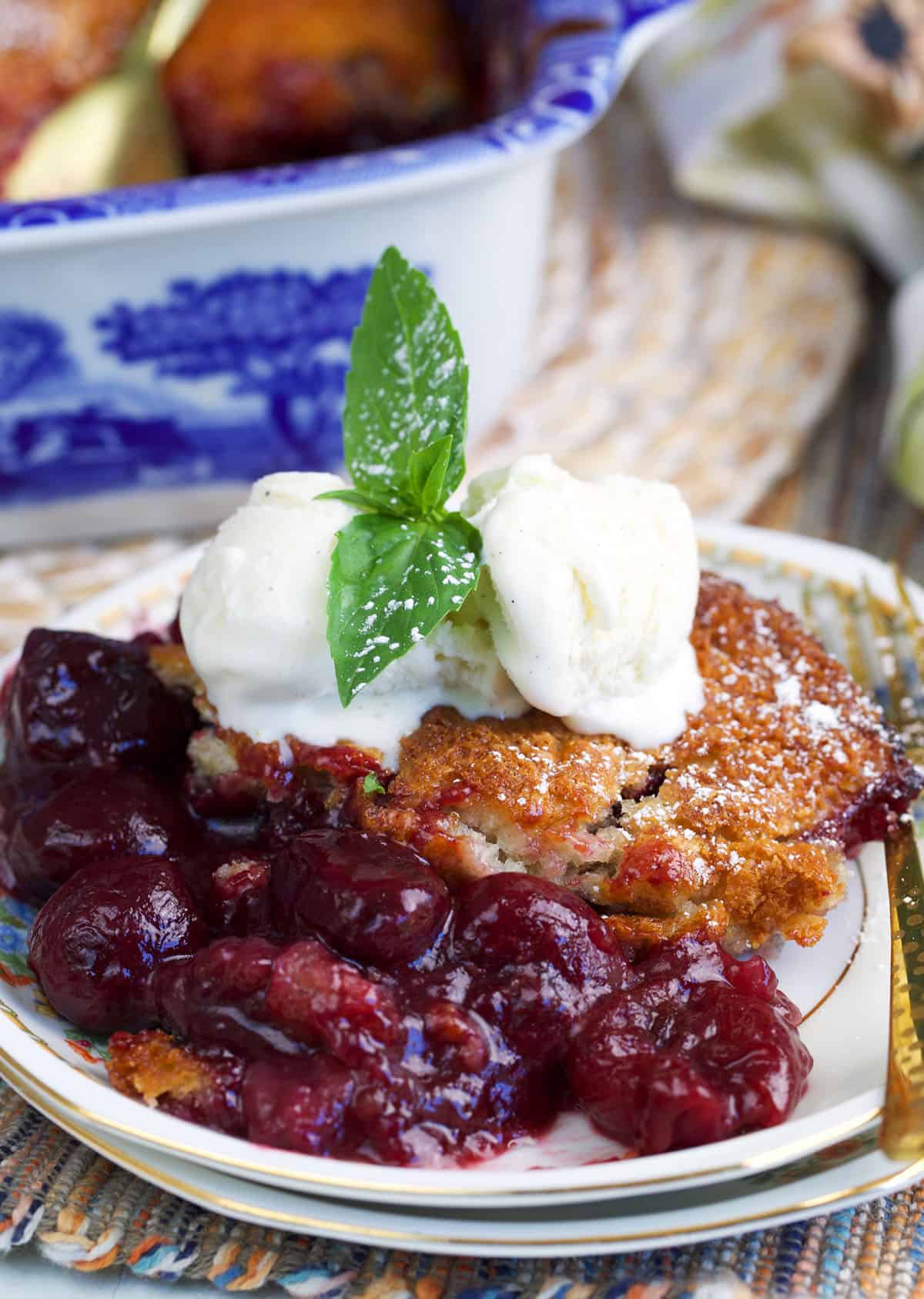 Cherry cobbler on a white dessert plate topped with two scoops of vanilla ice cream and a sprig of mint.
