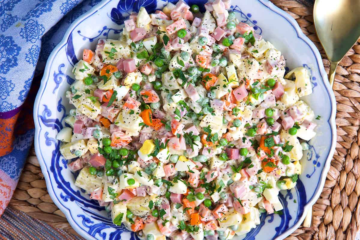 Russian Olivier Salad with carrots, ham, egg and peas in a blue and white serving bowl
