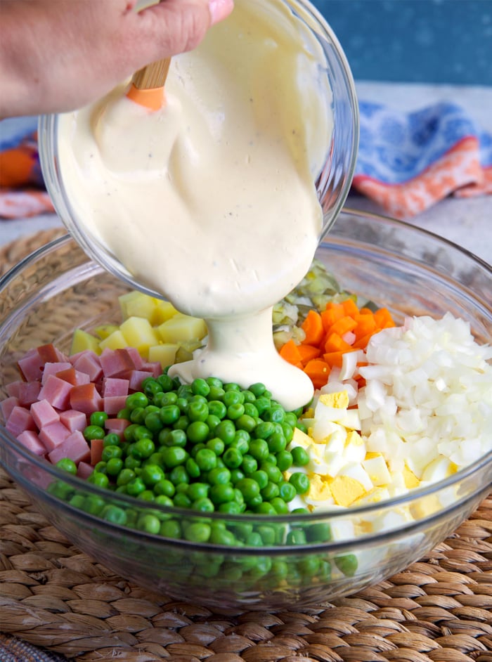 dressing being poured over ingredients for Russian salad in a glass bowl