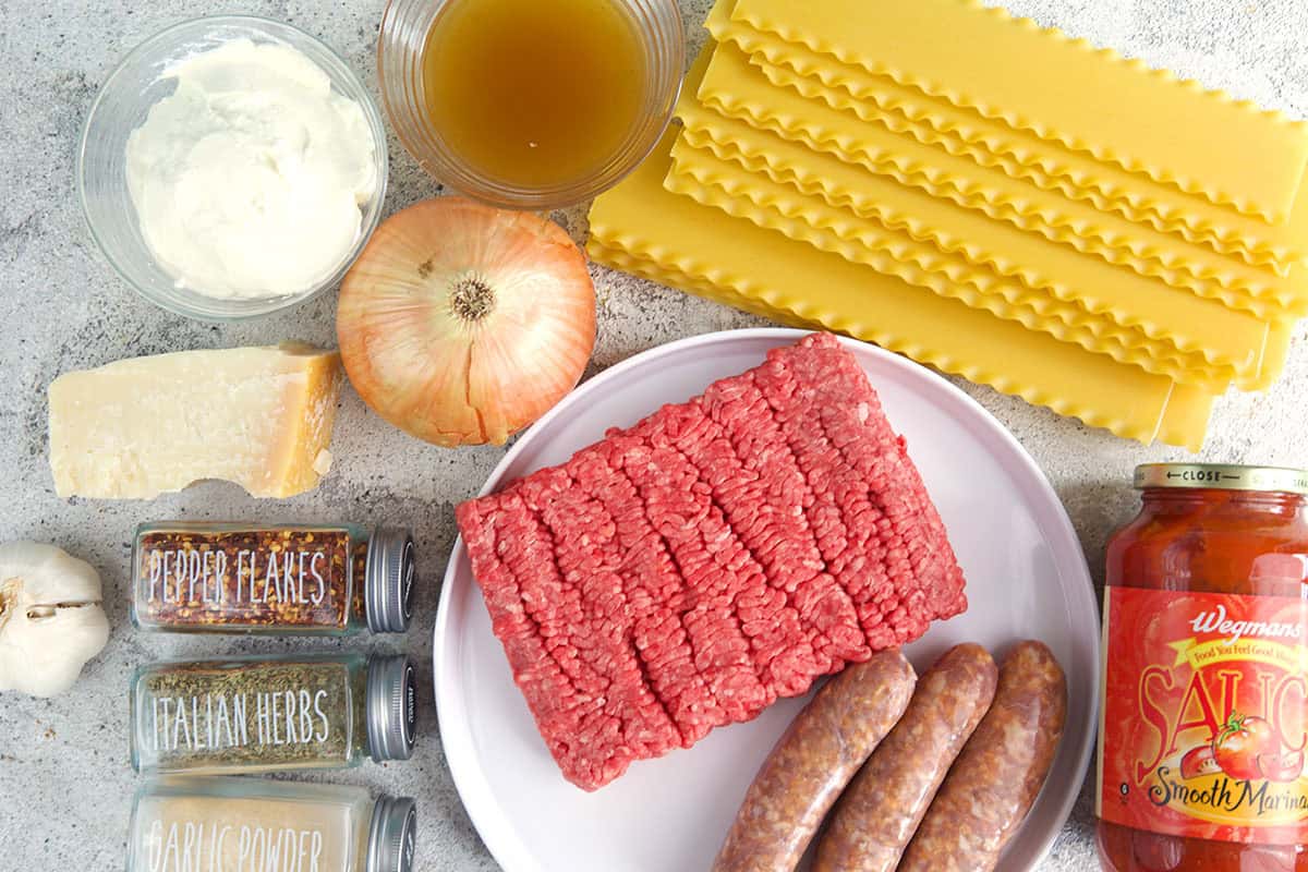 Ingredients for sheet pan lasagna, noodles, ground beef sausage, marinara, cheese, spiced, onion and chicken stock.