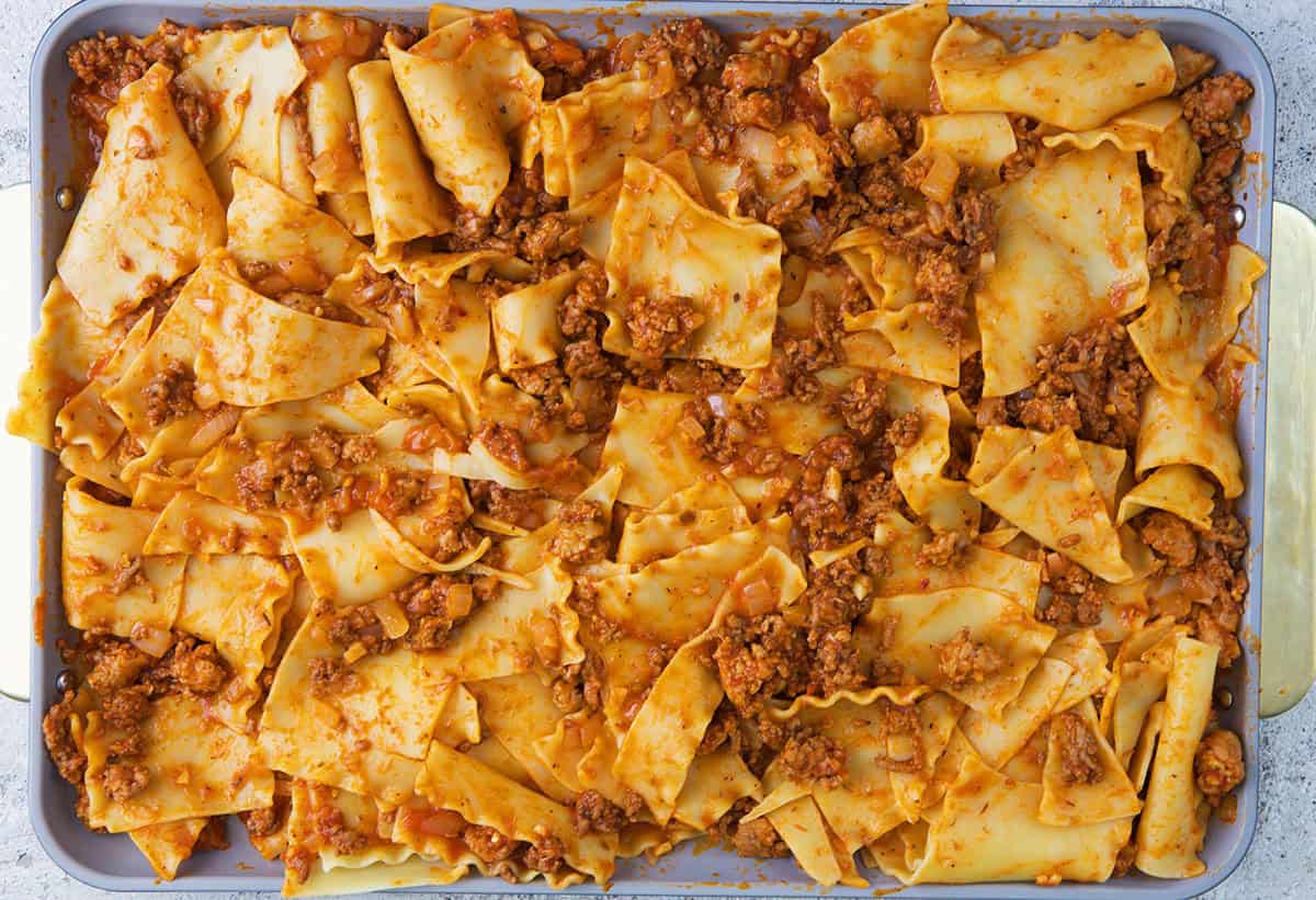 Broken lasagna noodles tossed with meat sauce on a sheet pan