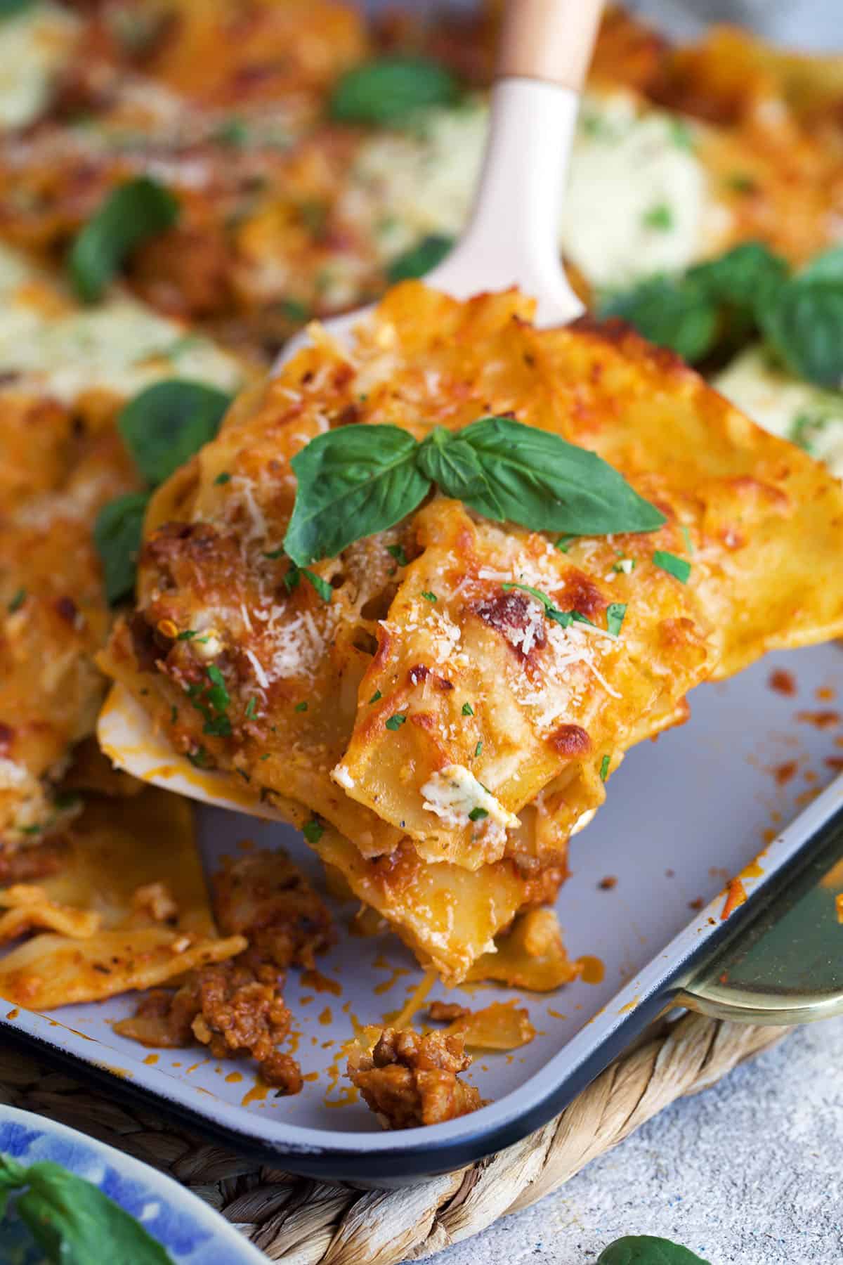 Sheet Pan Lasagna with crispy cheesy edges being served with a spatula