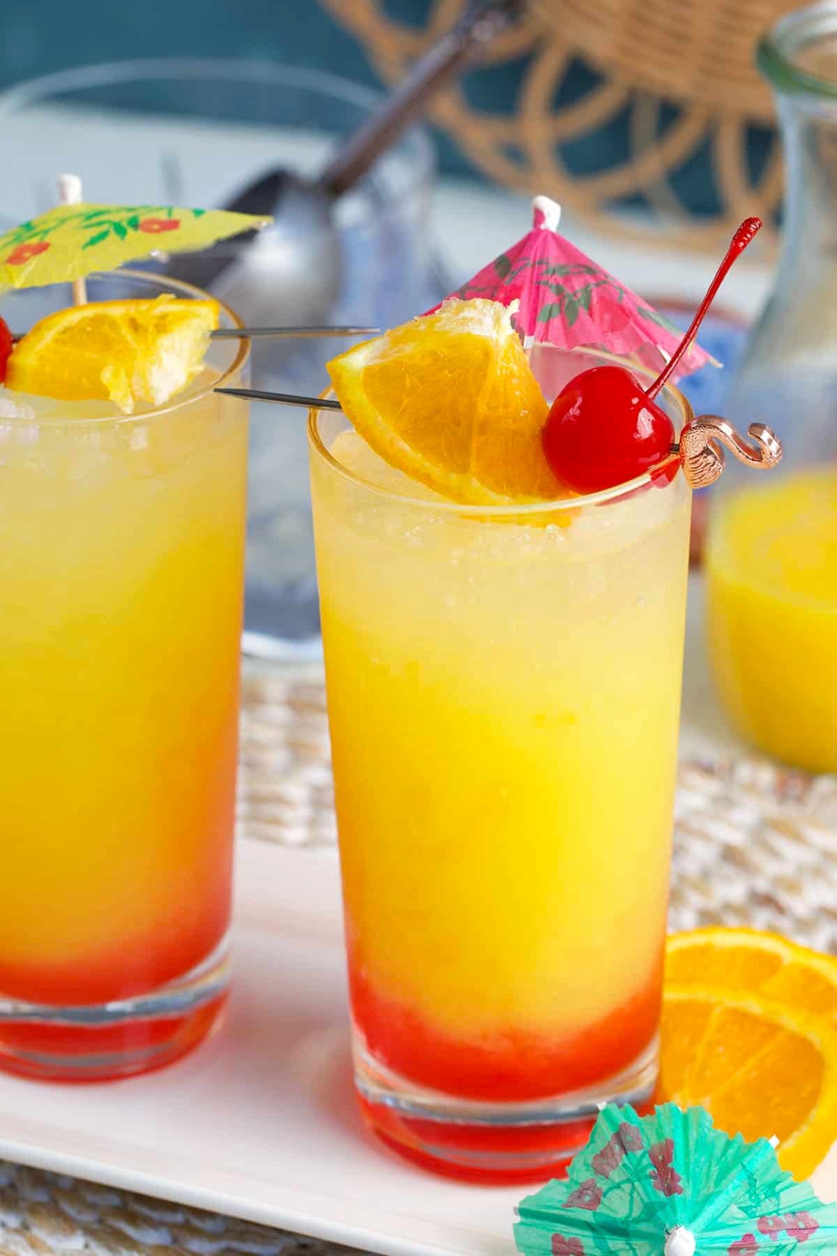Tequila sunrise drink on a white platter with a pink drink umbrella.