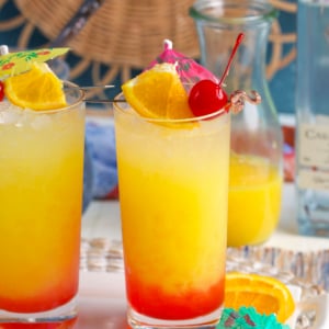 Tequila Sunrise cocktail in a collins glass with an orange slice, cherry and drink umbrella on top